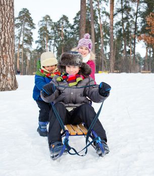 Cute three kids on sleds in snow forest. Focus on the boy