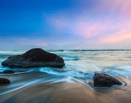 Tropical beach vacation background - waves and rocks on beach of sunset