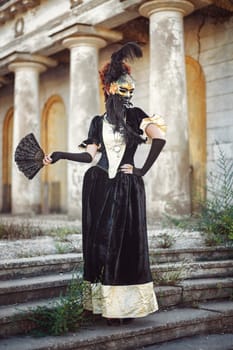 Portrait of red-haired woman holding a mask shot against the background of columns