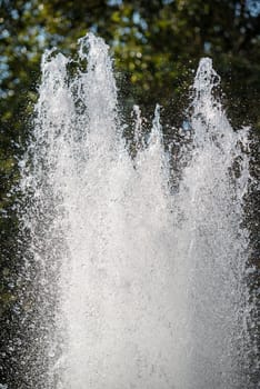 Splashes of fountain water on a sunny day with green trees in the background