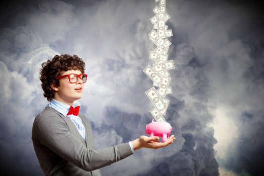 Image of young businessman in red glasses holding moneybox