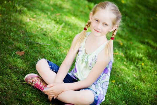 Image of little cute girl sitting on grass in park