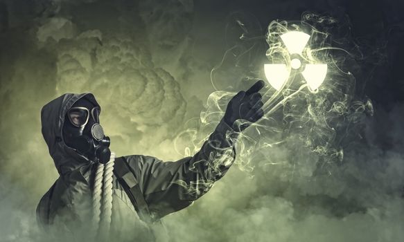 Man in respirator against nuclear background touching symbol. Pollution concept