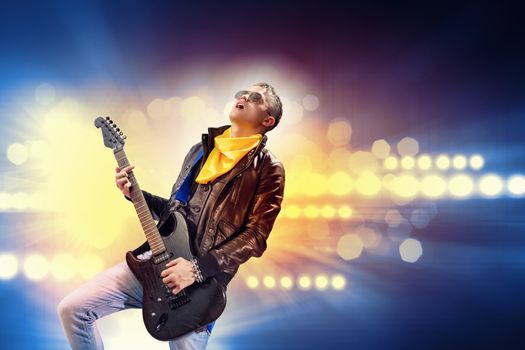 Young man, rock musician in jacket playing guitar