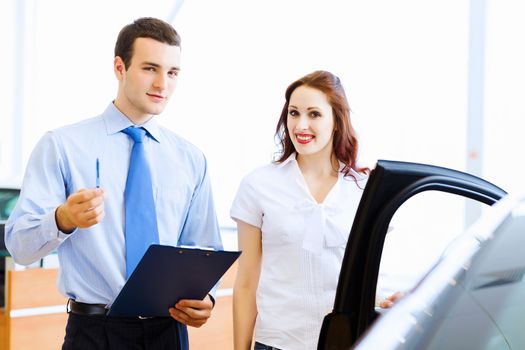 Attractive woman at car salon with consultant choosing a car