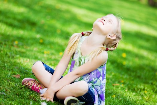 Image of little cute girl sitting on grass in park