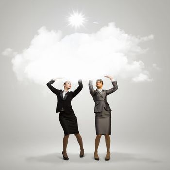 Image of two businesswomen holding clouds above head