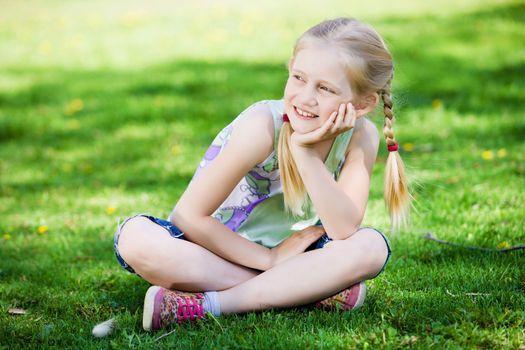 Image of little cute girl sitting on grass in park