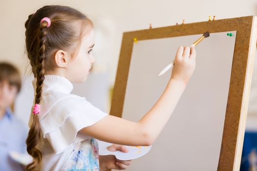 Little cute girl with paint brush and easel