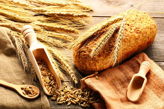 Rye spikelets and bread on wooden background