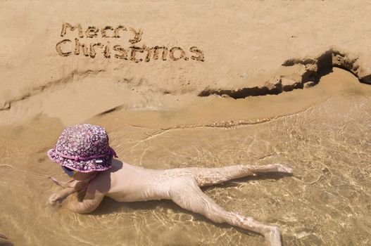 Merry Christmas written in the sand and baby in the water