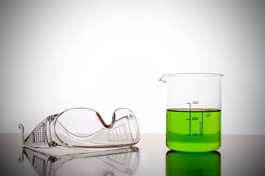 Measuring glass with green liquid and safety glasses, goggles in a chemical lab