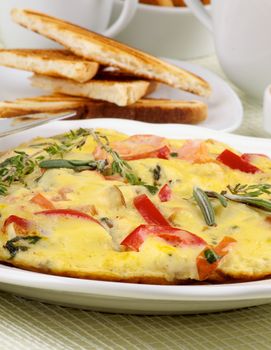 Delicious Omelet with Vegetables on Heap of Toasts and Dishware background closeup