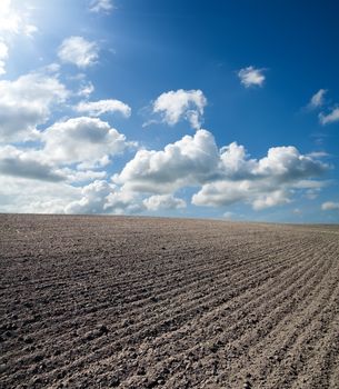 black ploughed field under blue cloudy sky