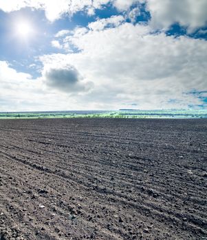 black ploughed field under blue cloudy sky