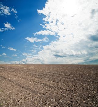 black ploughed field under blue cloudy sky