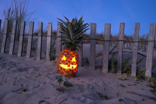 Jack o lantern made out of pinapple glowing at dark on beach