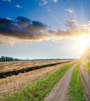 sunset over field and rural road with dramatic sky