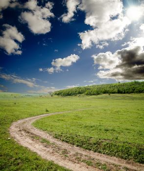 dirty road goes to horizon under cloudy sky with sun