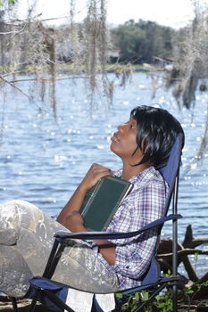 A lovely young woman looks away from her book at the waterfront.