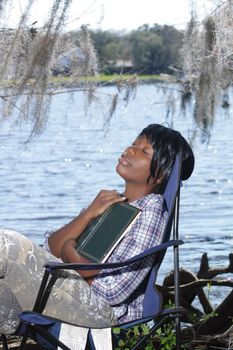 A lovely young woman who appears to be sleeping or pondering her book at the waterfront.