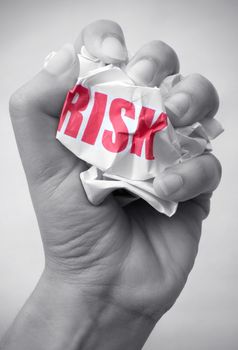 Hand squashing a crumpled piece of paper with the word risk 