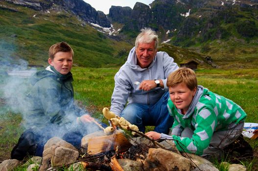 A father and two boys making twistbread on a bonfire