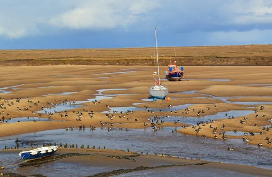 A landscape image showing boats at low tide on the Norfolk coast.