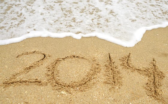 Bringing in the new year with 2014 written in sand on the beach