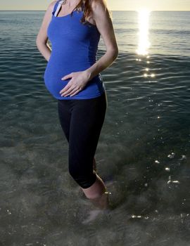pregnant woman holding stomach standing in ocean at beach