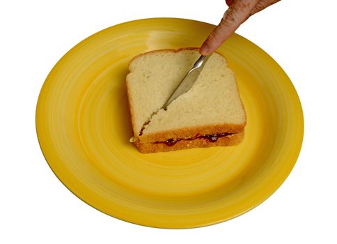 slicing peanut butter and jelly sandwich with a knife on a yellow plate