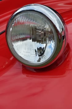 Detail of car headlamp on red in portrait