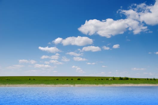 water and green field under deep blue cloudy sky