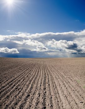 black ploughed field under blue cloudy sky with sun