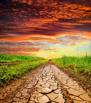 cracked rural road in green grass and cloudy sky