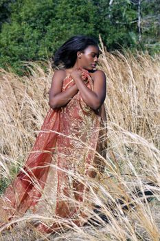 A lovely young black woman outdoors, standing in tall grass, wrapped in translucent fabric