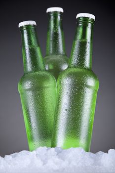 Three green beer bottles sitting on ice over a gray background.