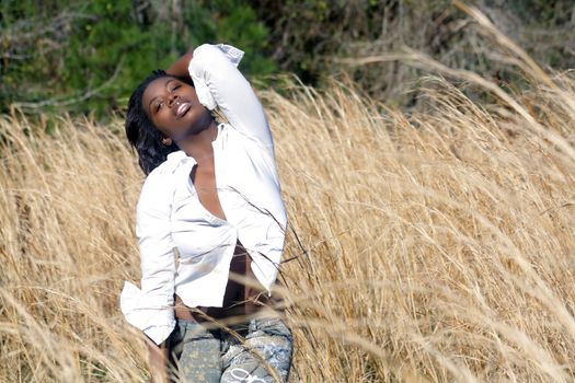 A lovely young black woman outdoors, standing in tall grass.  Generous copyspace on frame right.