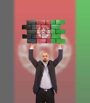 Businessman holding a large piece of a brick wall, flag of Afghanistan, isolated on national flag