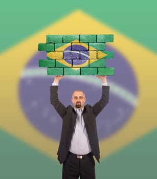 Businessman holding a large piece of a brick wall, flag of Brazil, isolated on national flag