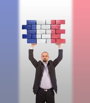 Businessman holding a large piece of a brick wall, flag of France, isolated on national flag