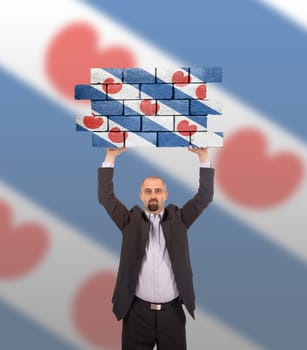 Businessman holding a large piece of a brick wall, flag of Friesland, isolated on national flag