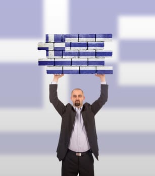 Businessman holding a large piece of a brick wall, flag of Greece, isolated on national flag