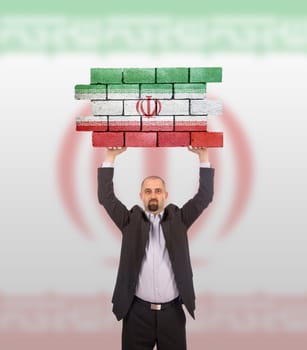 Businessman holding a large piece of a brick wall, flag of Iran, isolated on national flag