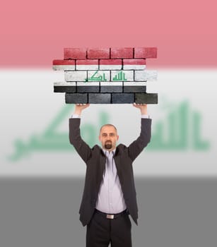 Businessman holding a large piece of a brick wall, flag of Iraq, isolated on national flag