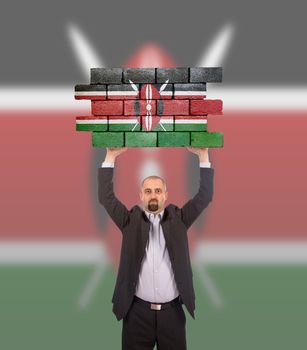Businessman holding a large piece of a brick wall, flag of Kenya, isolated on national flag