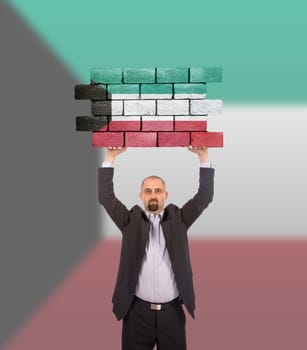Businessman holding a large piece of a brick wall, flag of Kuwait, isolated on national flag