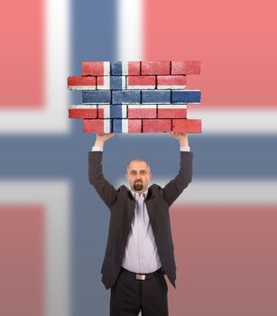 Businessman holding a large piece of a brick wall, flag of Norway, isolated on national flag