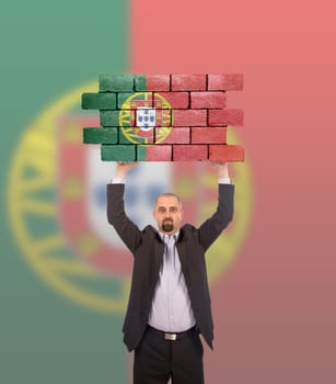 Businessman holding a large piece of a brick wall, flag of Portugal, isolated on national flag