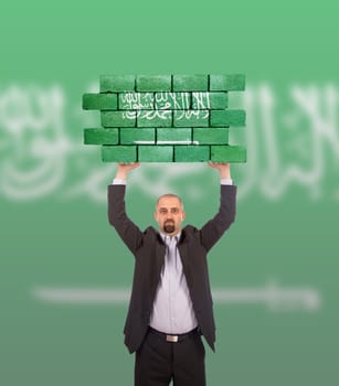 Businessman holding a large piece of a brick wall, flag of Saudi Arabia, isolated on national flag